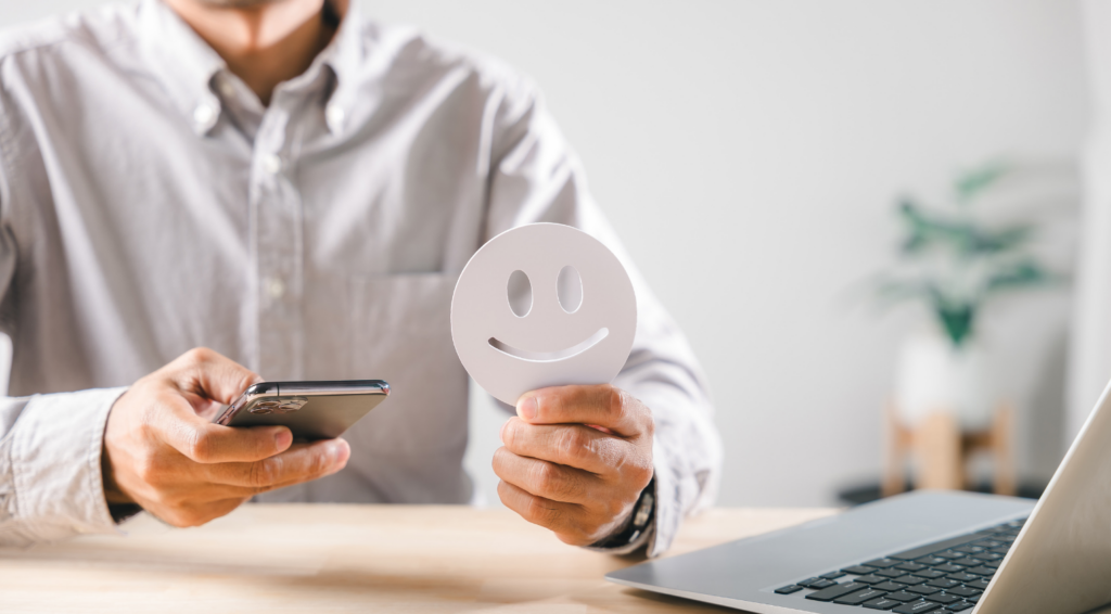 スマホを見ながら笑顔のアイコンを掲げる様子。出張買取エコの口コミを確認するイメージ