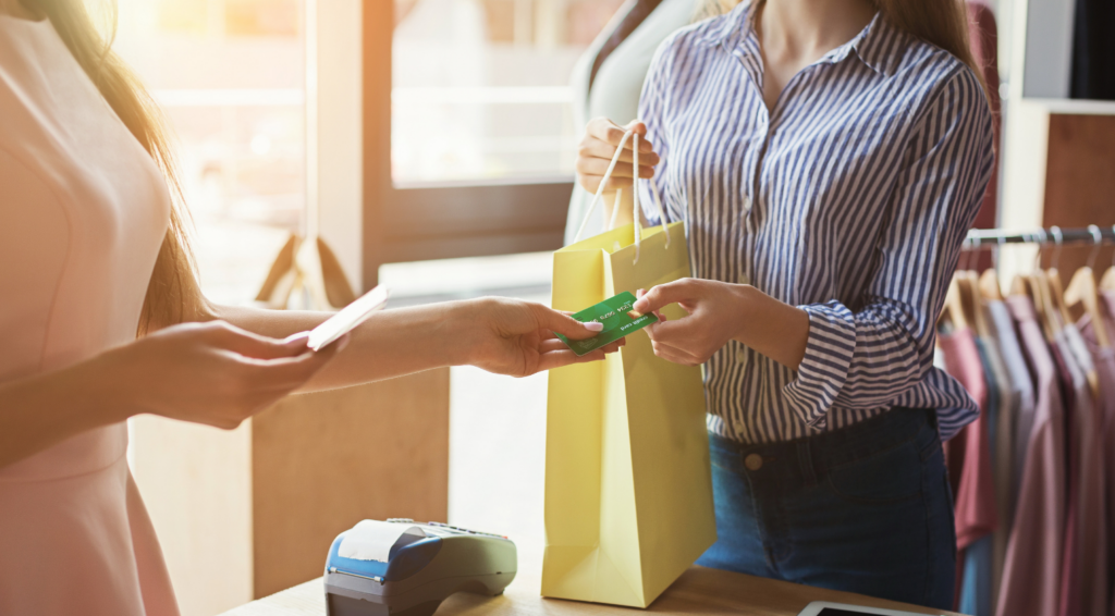 買い物袋を持つ店員とカードを渡す客の手元。出張買取エコの口コミで見かける取引イメージ